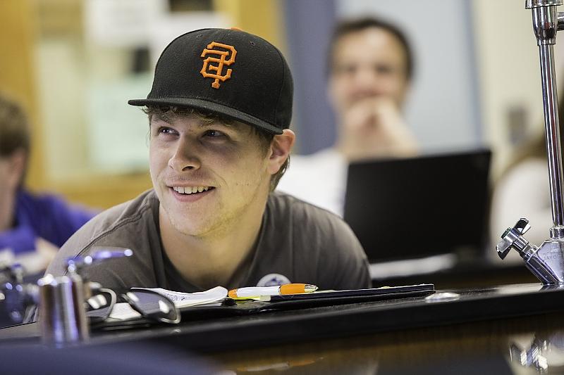 戴棒球帽的学生坐在科学实验桌旁微笑